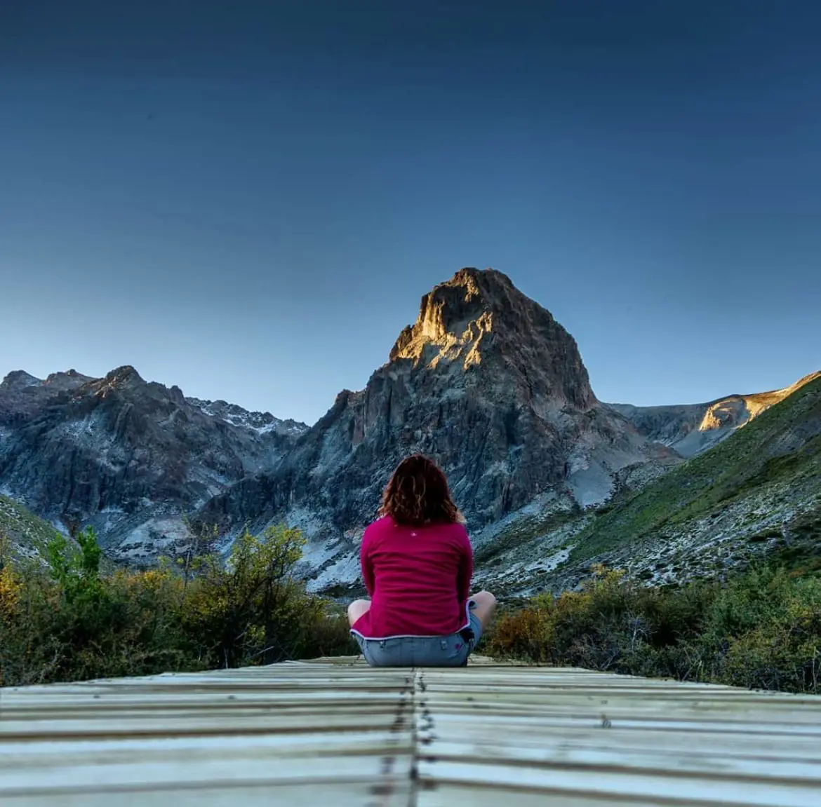 Persona contemplando una cumbre rocosa desde una pasarela de madera